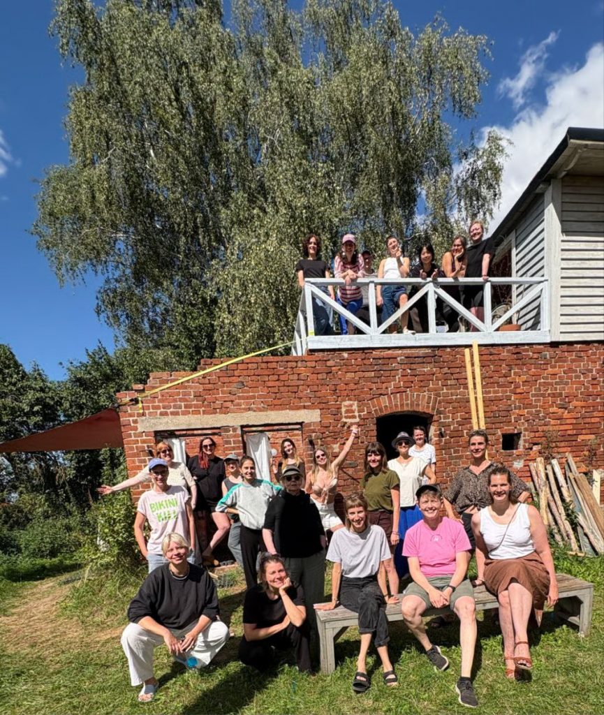 Auf dem Bild sind ca. 20 Menschen zu sehen, die vor einem Haus stehen und sitzen.